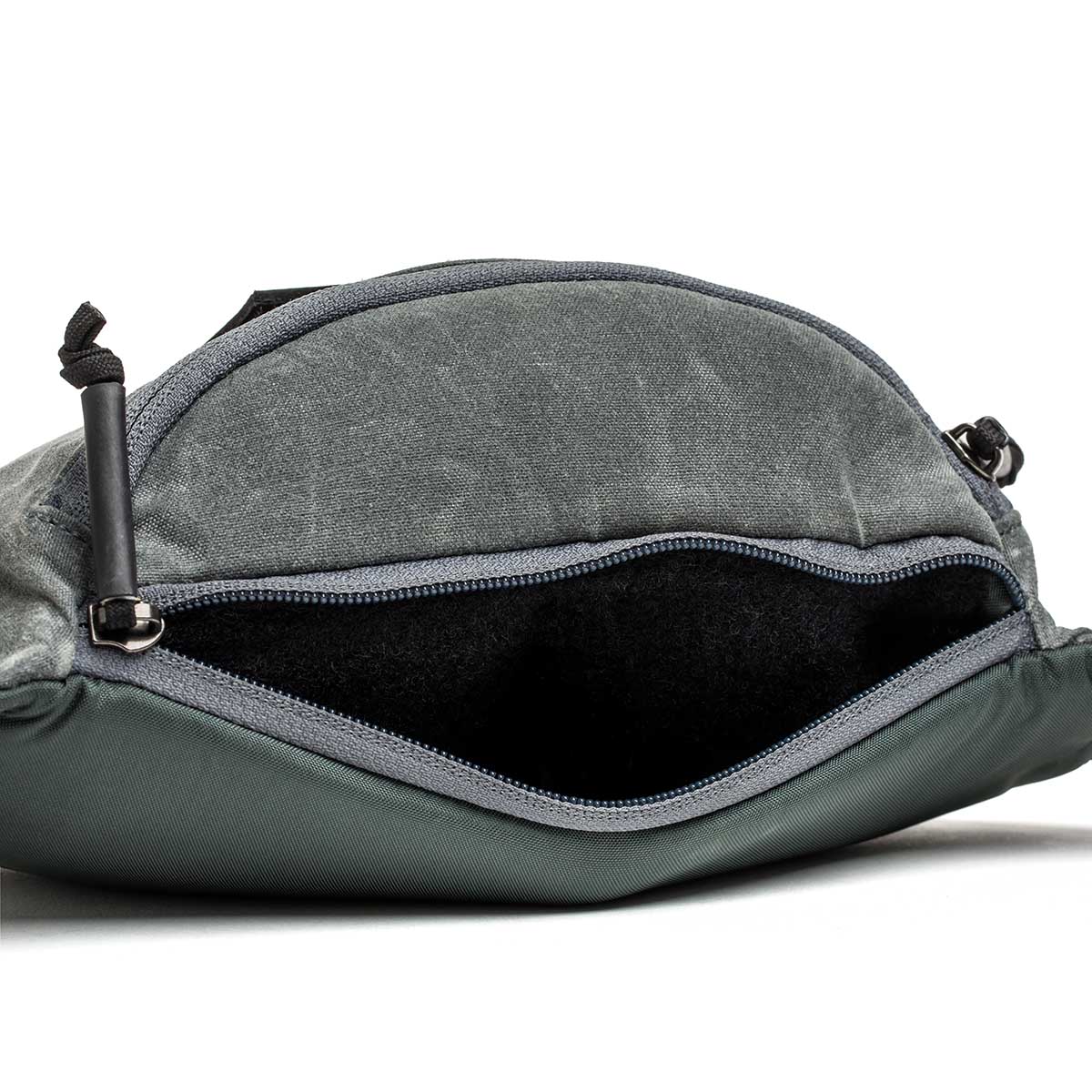 Open Tactical Fanny Pack - Waxed Canvas in gray fabric with silent zipper pulls, revealing its empty black interior against a white background.