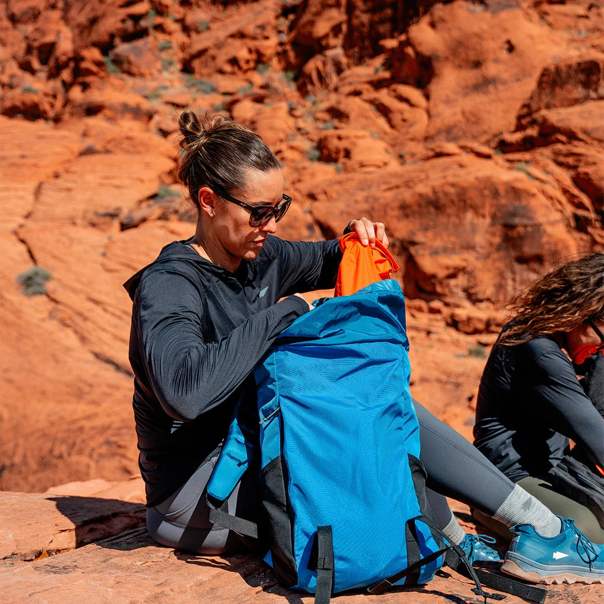 Person packing a blue GORUCK backpack on red rock outdoors, rucking gear adventure