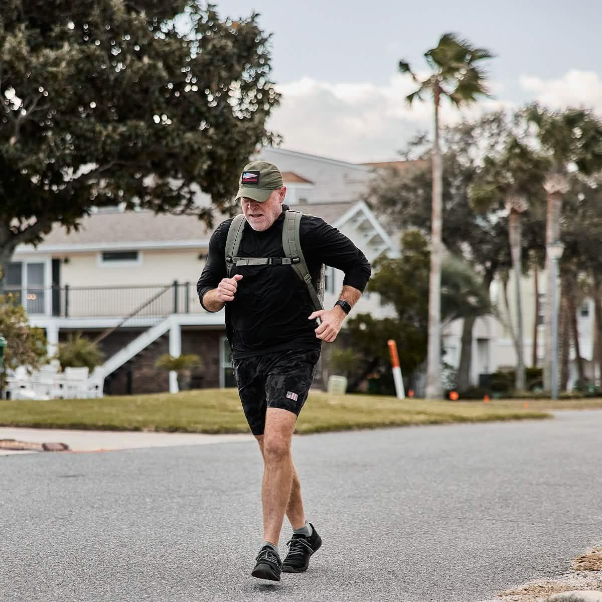 Man rucking in GORUCK ToughMesh black hoodie, shorts, and rucksack outside suburban houses