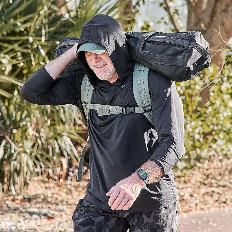 Man wearing black ToughMesh hoodie and cap carrying weighted bag on shoulders outdoors in sunny setting