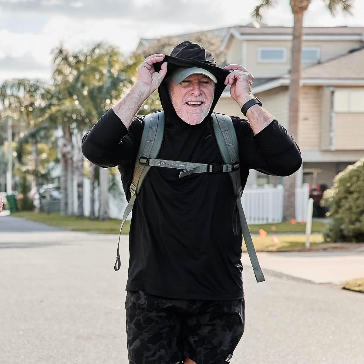 Man wearing GORUCK ToughMesh Hoodie in black with backpack outdoors on suburban street