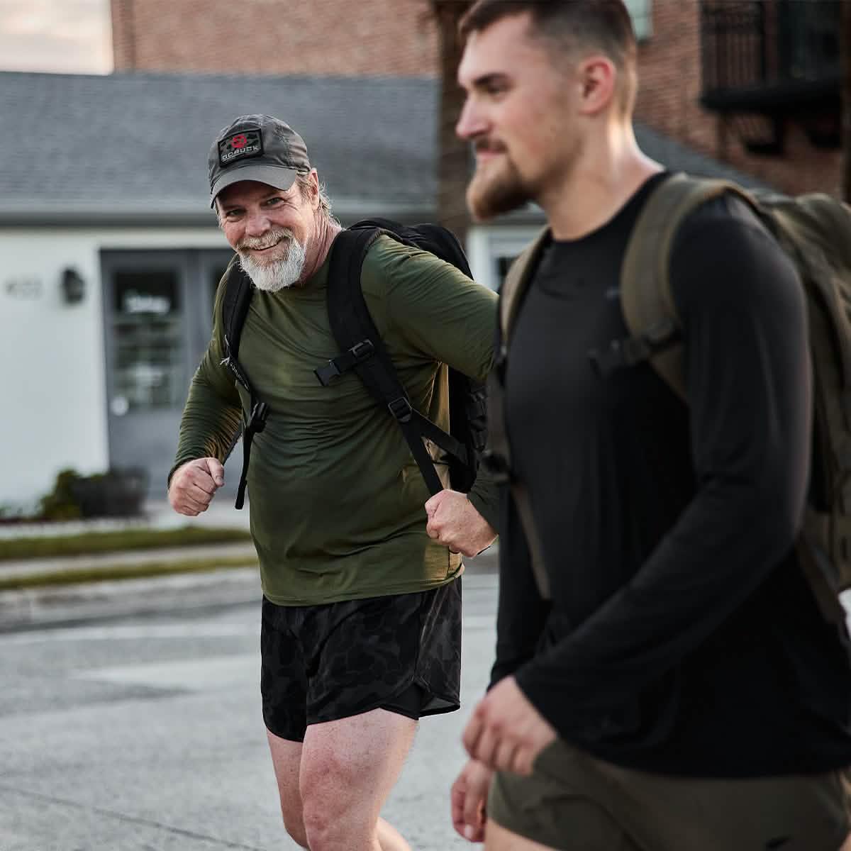 Two men wearing GORUCK backpacks and athletic gear rucking outdoors on a city street.