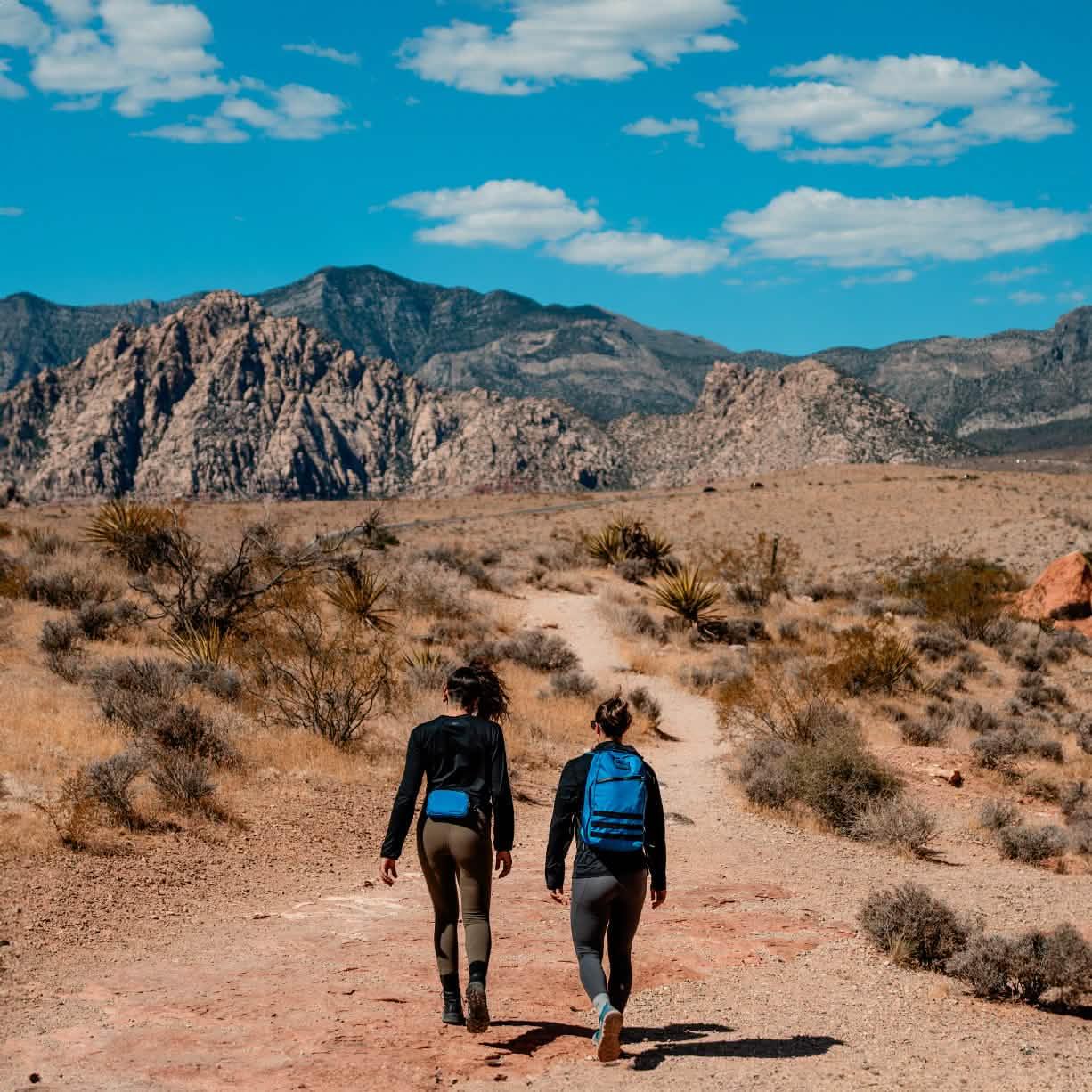 Two people hiking in desert mountains with GORUCK rucksacks under blue sky