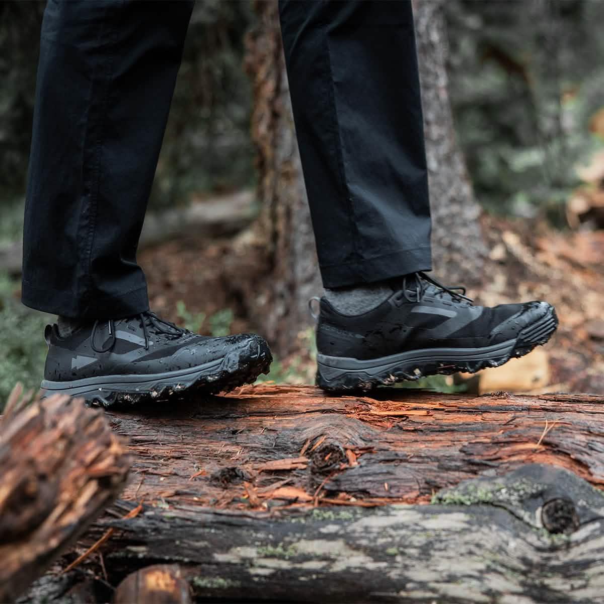 Close-up of feet wearing black trail running shoes and charcoal Merino socks standing on a log in a forest setting