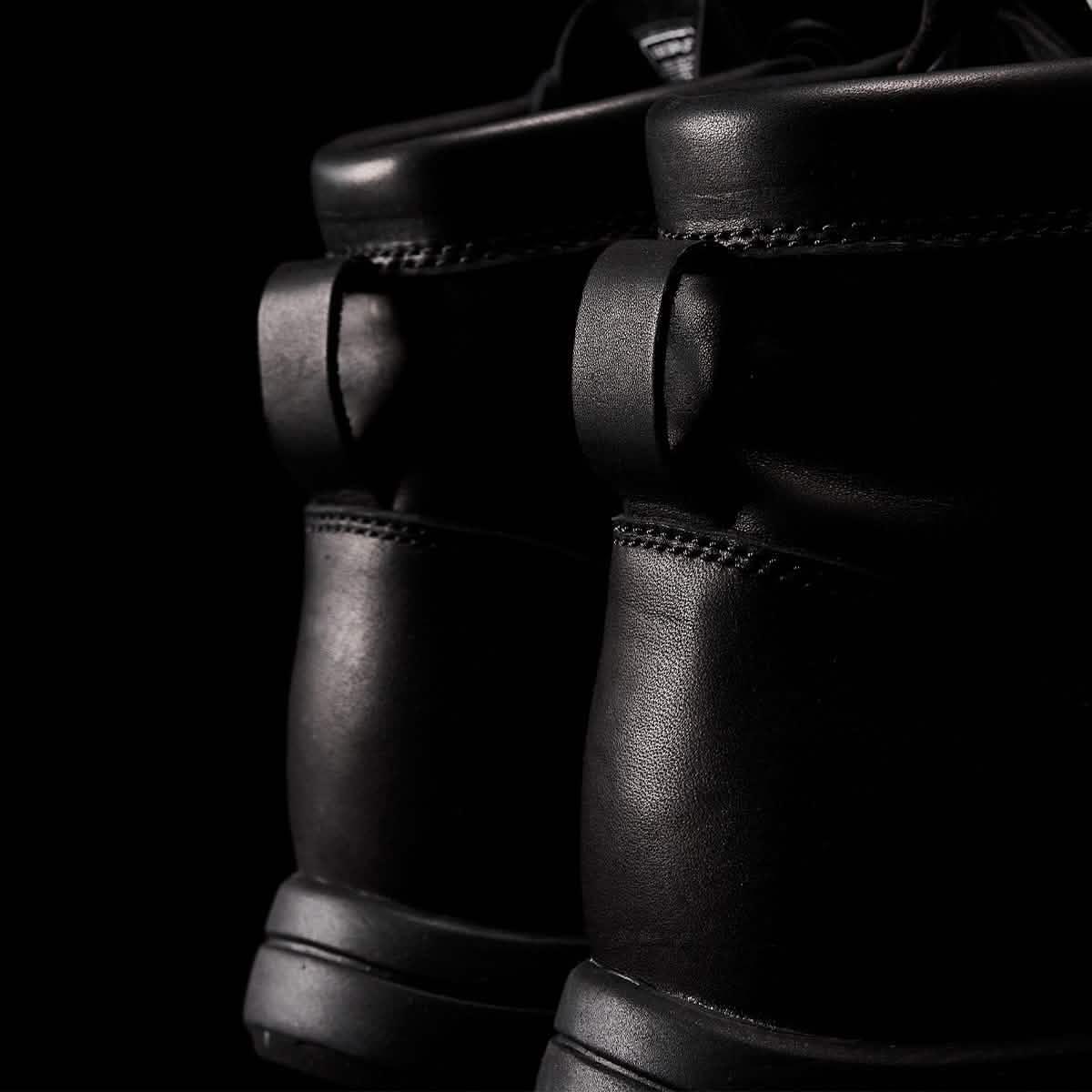 Close-up of black leather rucking boots with sturdy stitching against a dark background