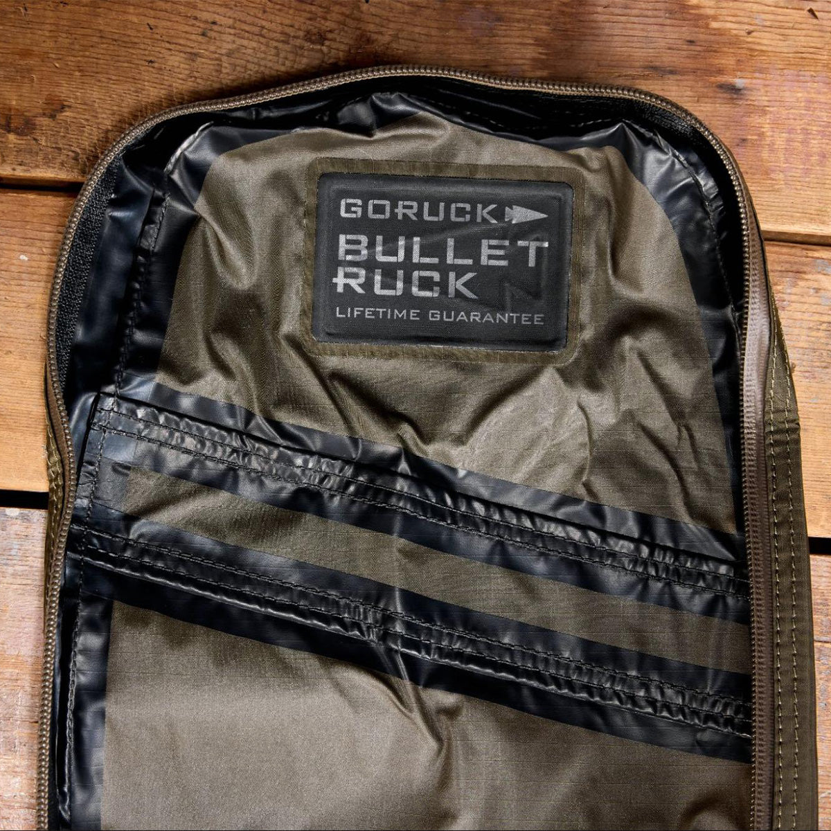 Open backpack showing label that reads “GORUCK BULLET RUCK LIFETIME GUARANTEE” on green fabric.