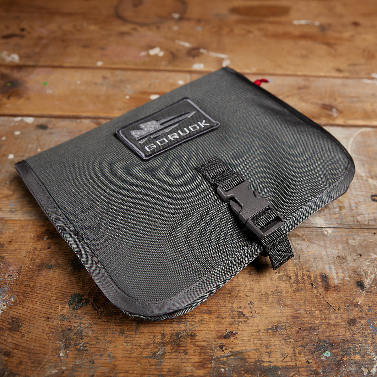The dark gray Wire Dopp pouch from GORUCK, made with durable CORDURA and featuring a buckle closure, sits closed on a worn wooden surface—perfect for keeping your travel essentials organized.