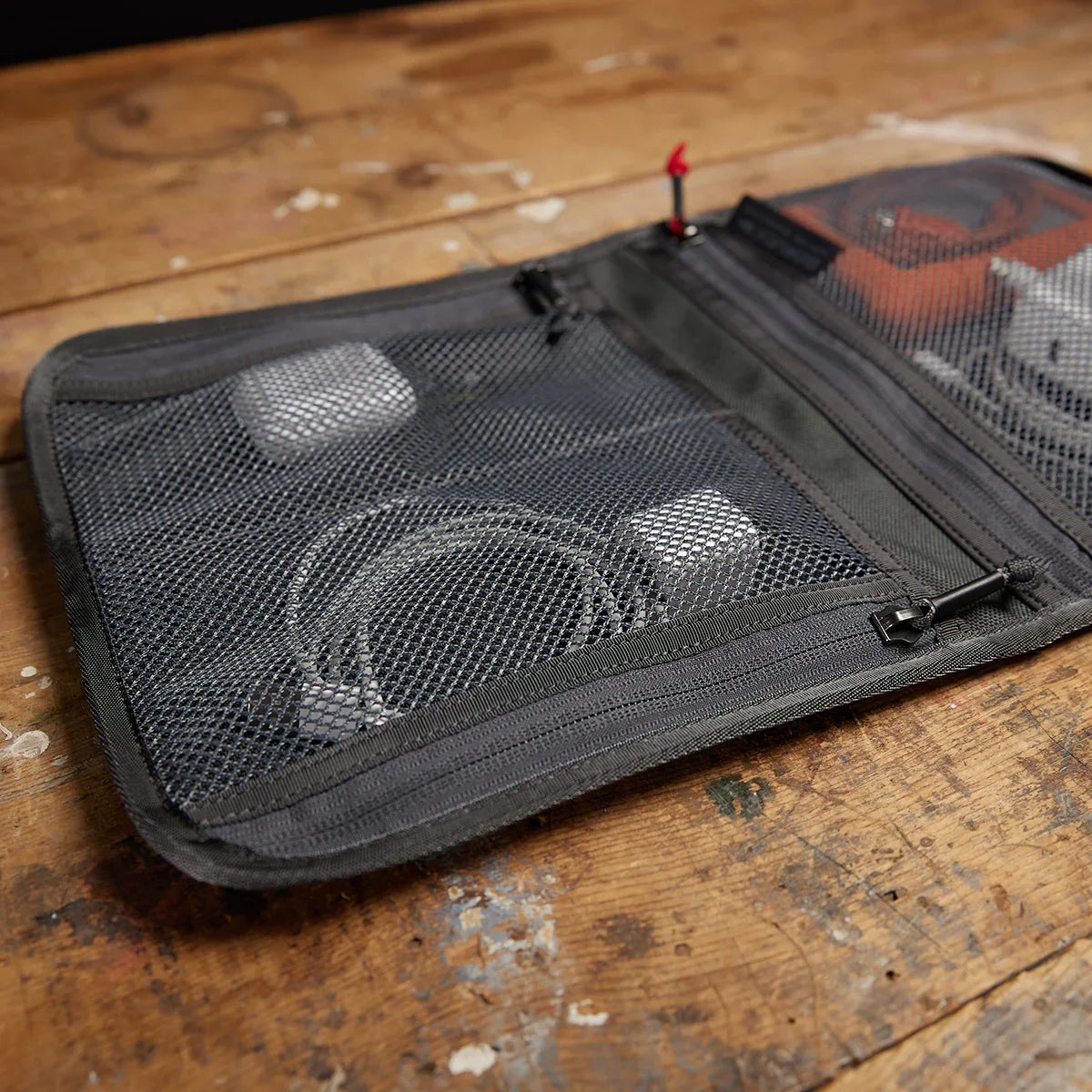 GORUCK Wire Dopp Kit Armor Grey open on wood surface showing mesh compartments with cables and gear inside