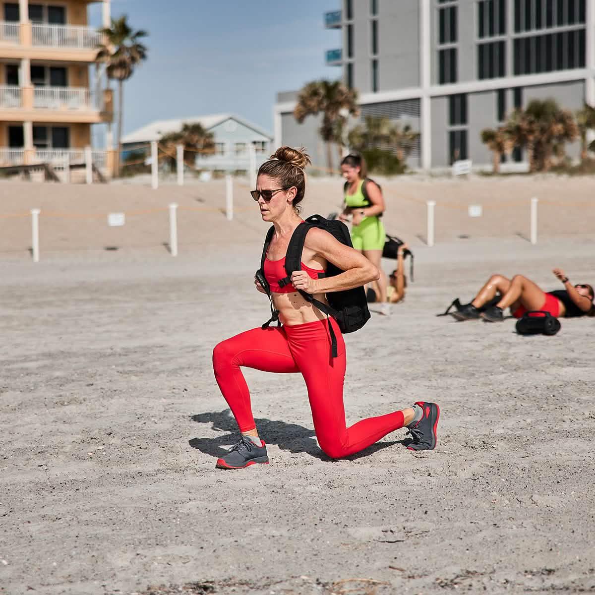 Woman training on beach in red activewear, wearing GORUCK ballistic trainers and rucksack