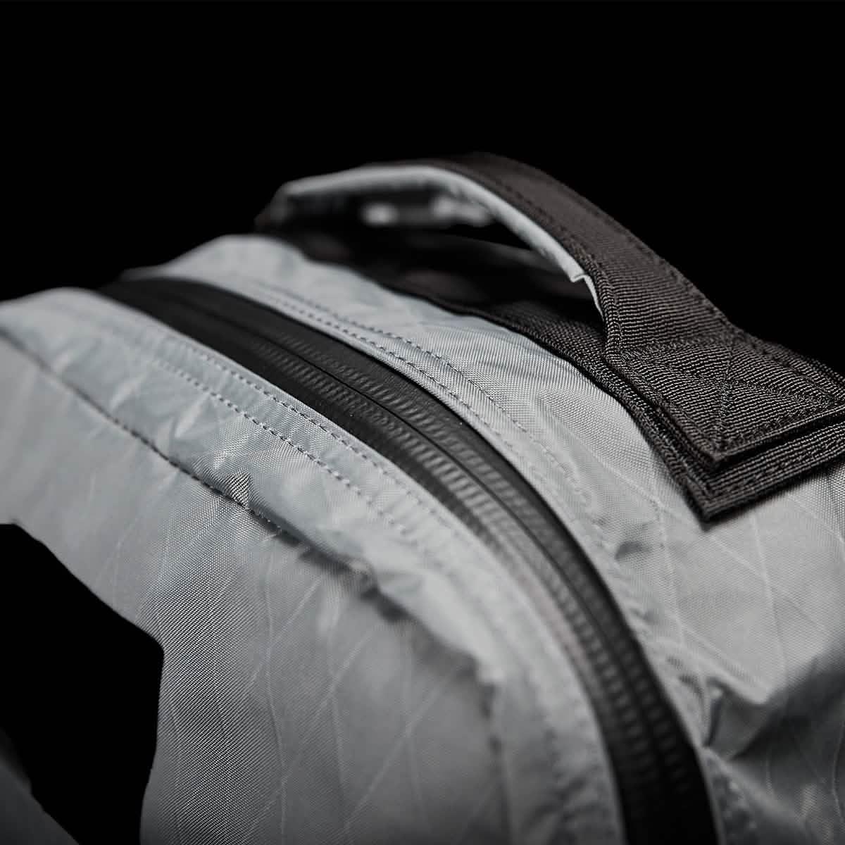 Close-up of sturdy gray backpack fabric with black zipper and handle against black background