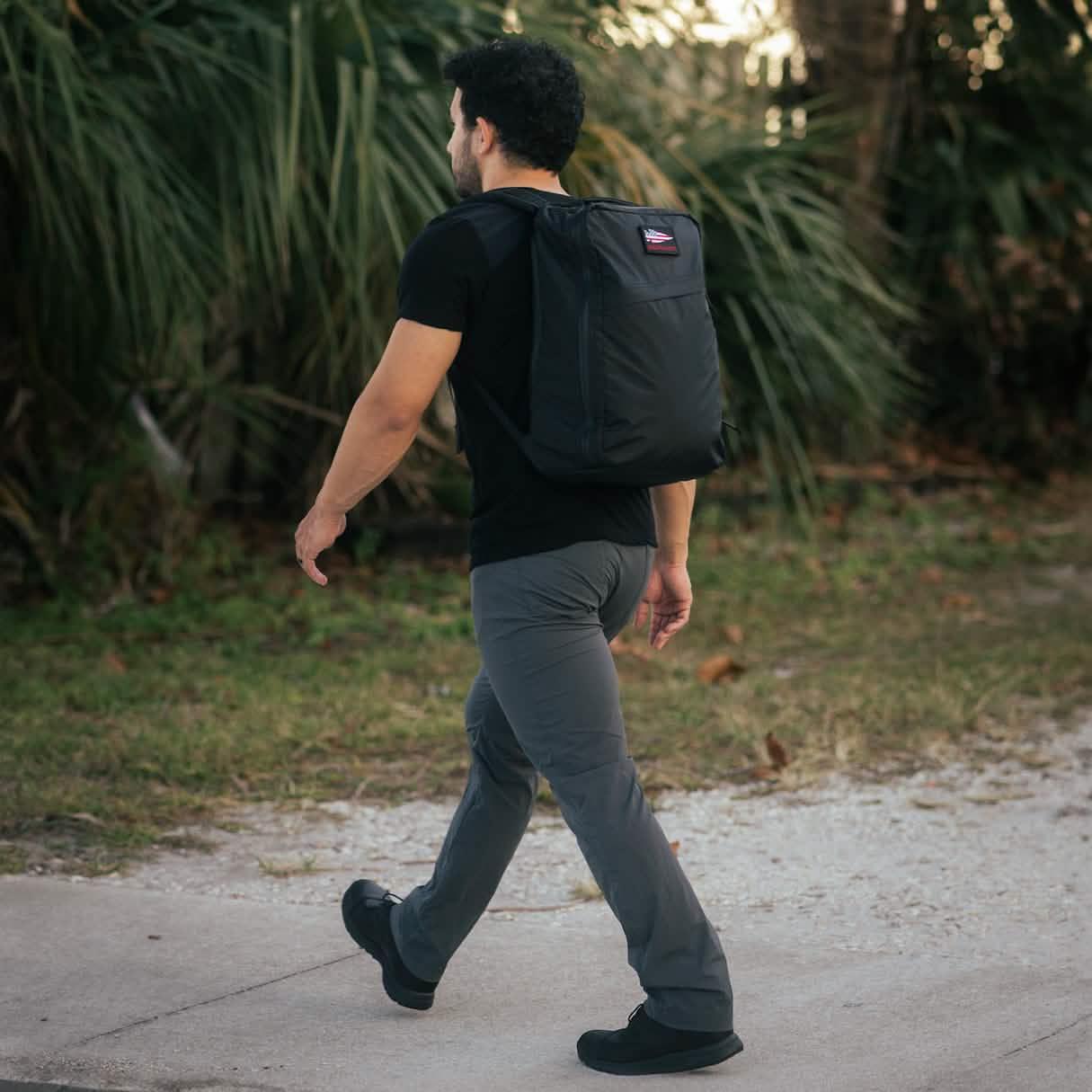 Man walking outdoors wearing GORUCK Xpac 21L black rucksack with an American flag patch