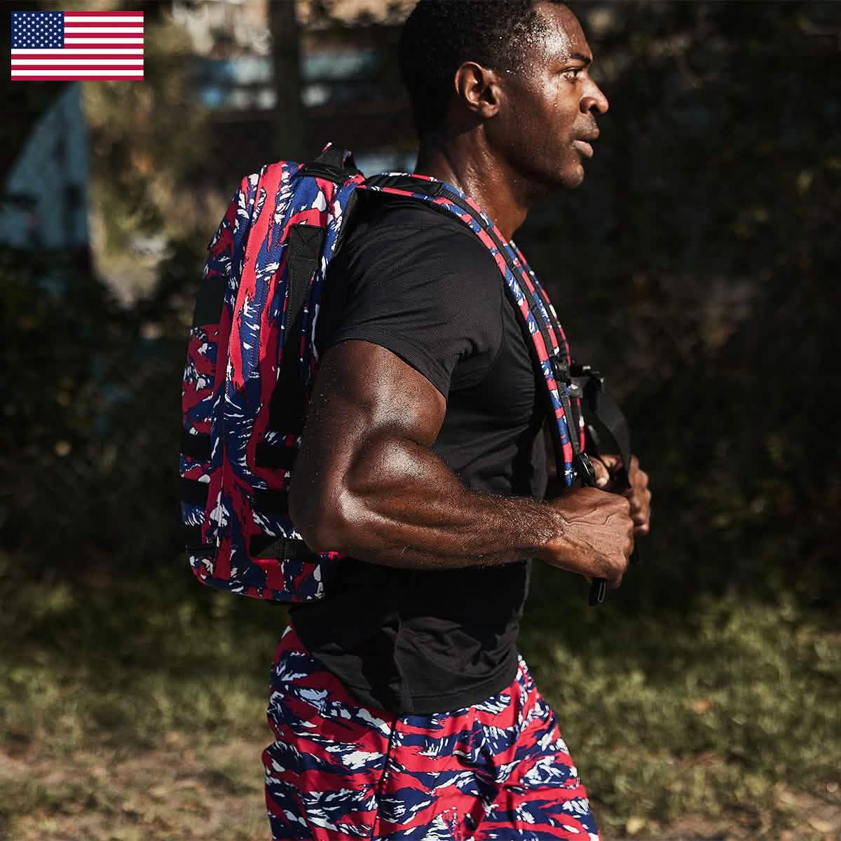 Athletic man sweating while rucking outdoors wearing red, white, and blue camo GORUCK backpack and matching shorts