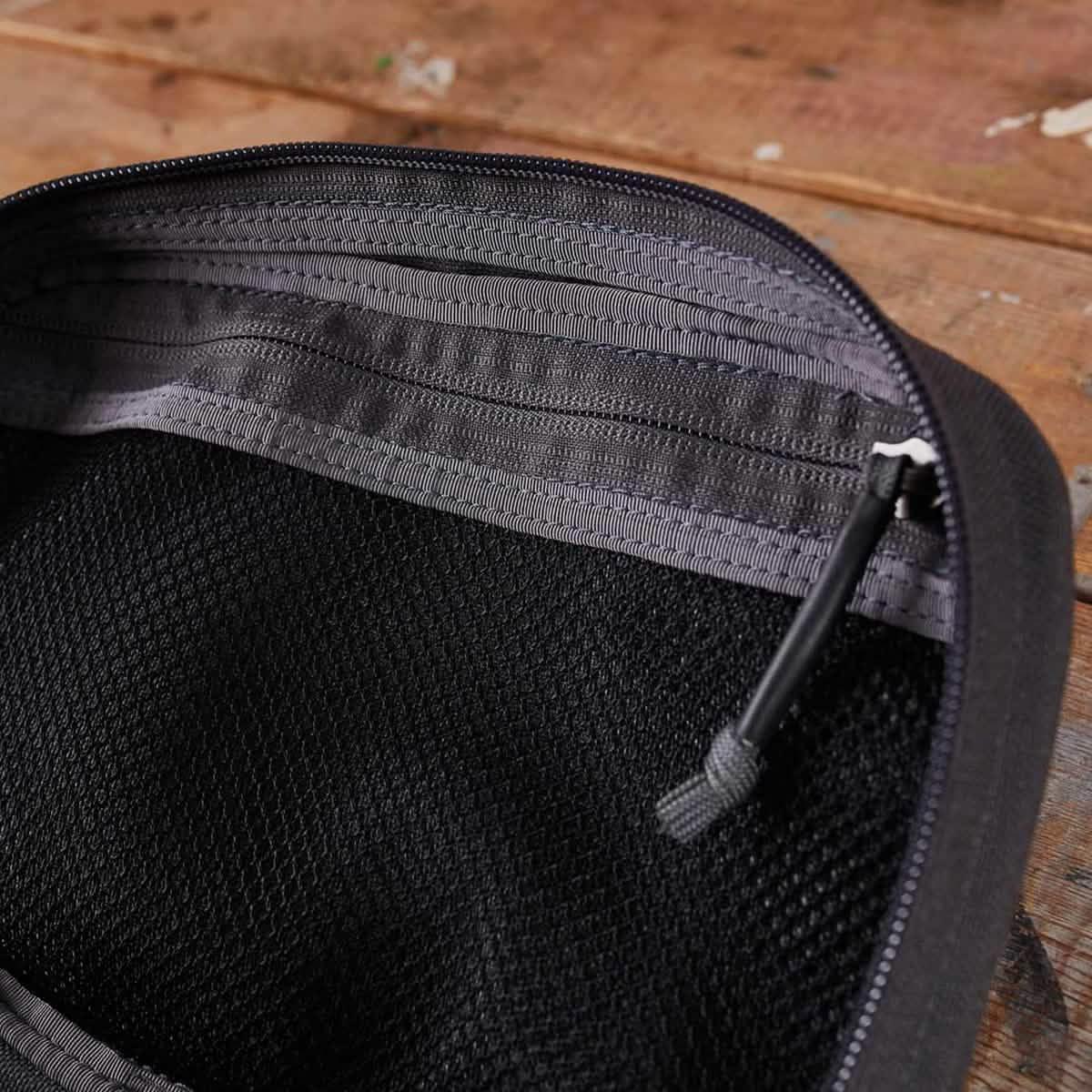 Close-up of black tactical pouch with mesh interior and gray zipper on wooden surface