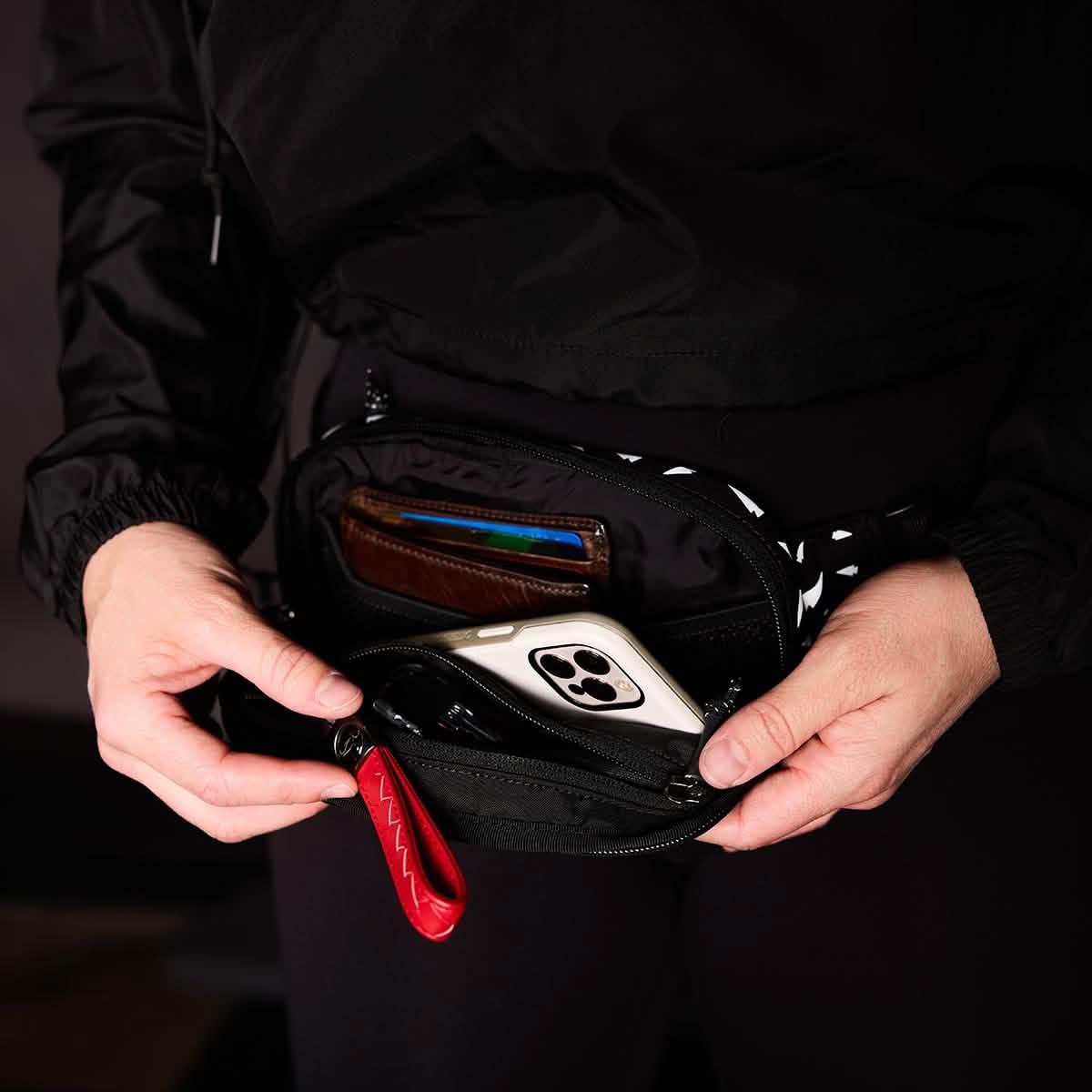 Person opening a black GORUCK belt bag with wallet and smartphone inside, showcasing durable rucking gear