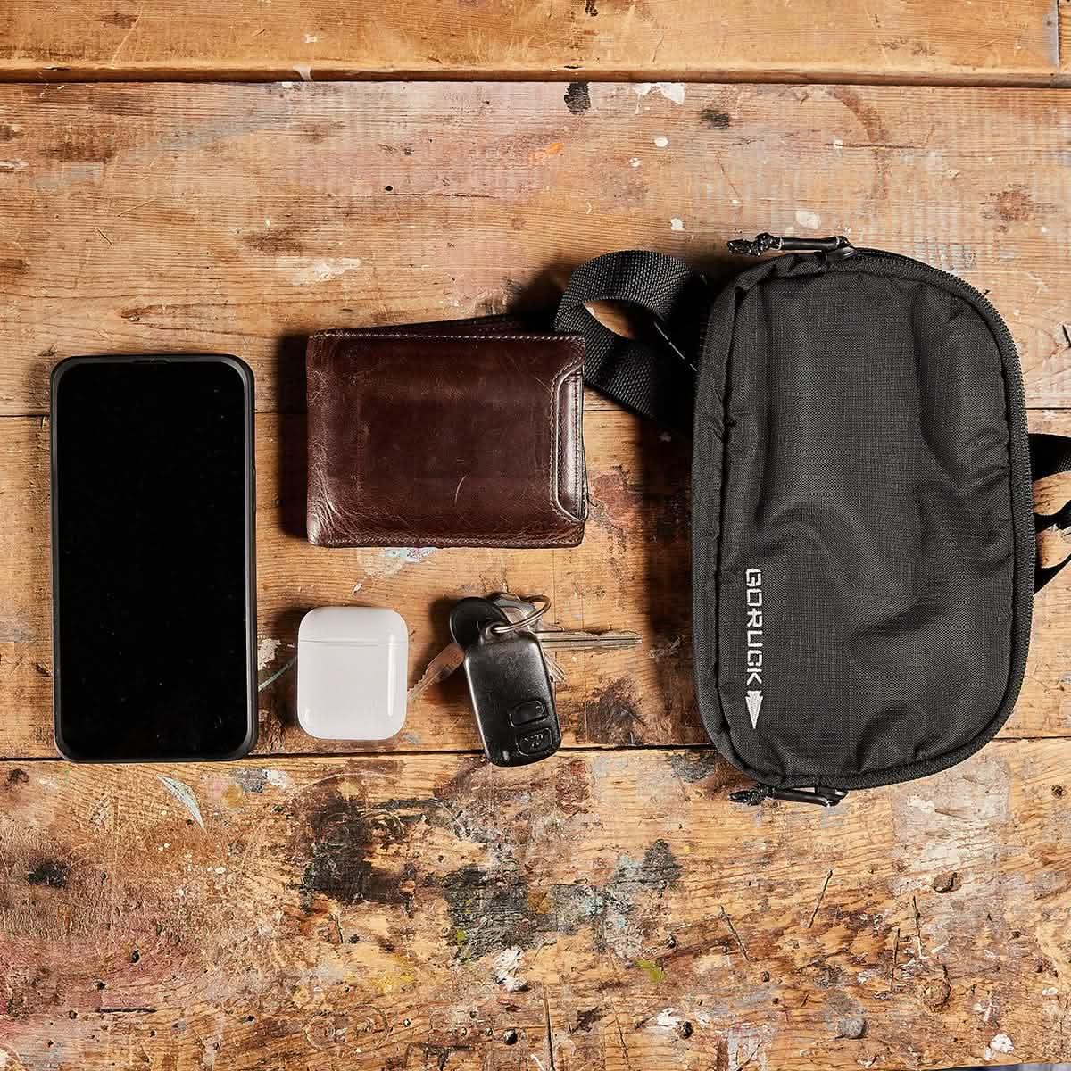 GORUCK belt bag on wooden table with phone, wallet, AirPods, and keys, everyday carry gear