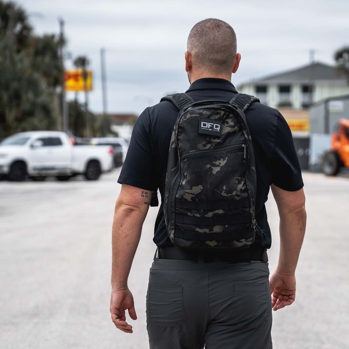 A man carrying the Bullet Ruck Classic - Ballistic Nylon Cordura backpack walks along a street with cars and buildings in the background.