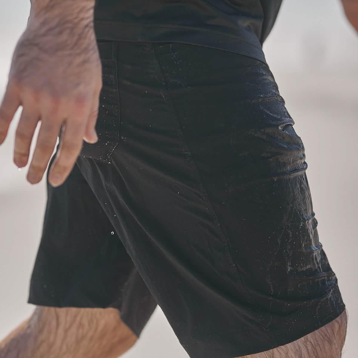 Close-up of a person wearing wet black GORUCK shorts with water droplets on fabric and visible legs