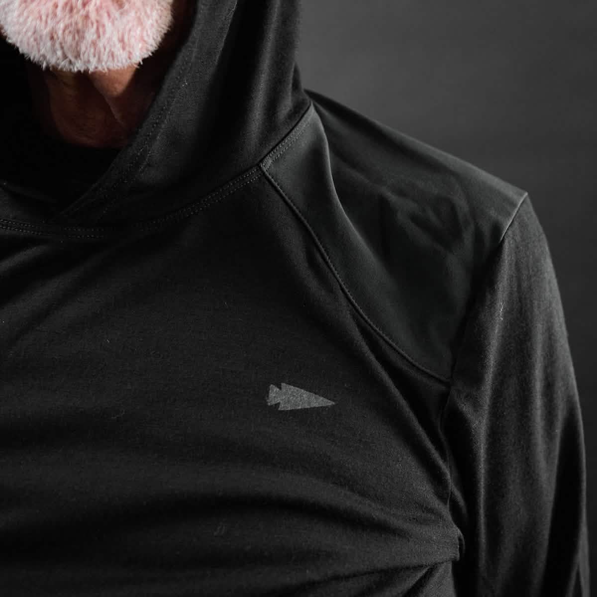 A close-up of a person wearing the GORUCK Men’s Commando Pullover - Merino Wool, featuring reinforced paneling and a small arrowhead logo on the chest. The face, partially visible with a white beard, is set against a dark background.