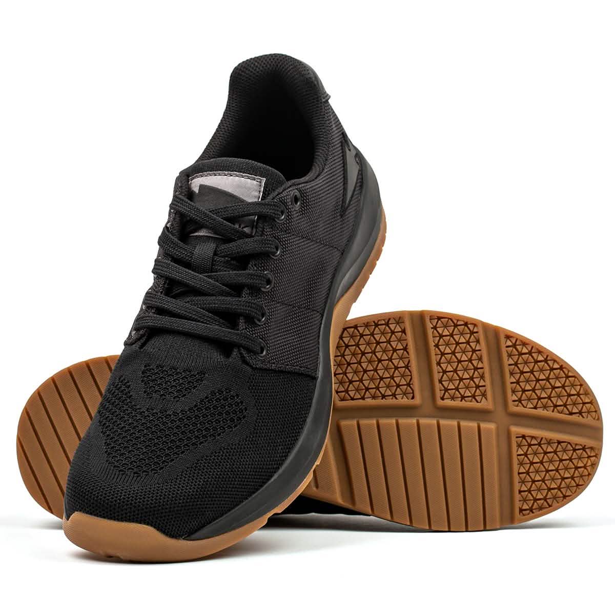 Introducing the Women's Ballistic Trainers in Black + Gum with Black Reflective Spearhead by GORUCK—a perfect choice for functional fitness enthusiasts. One shoe is shown upright while the other lies on its side, highlighting the intricate patterned tread. The mesh uppers and laces are fortified with CORDURA® Ballistic Nylon to ensure maximum durability.