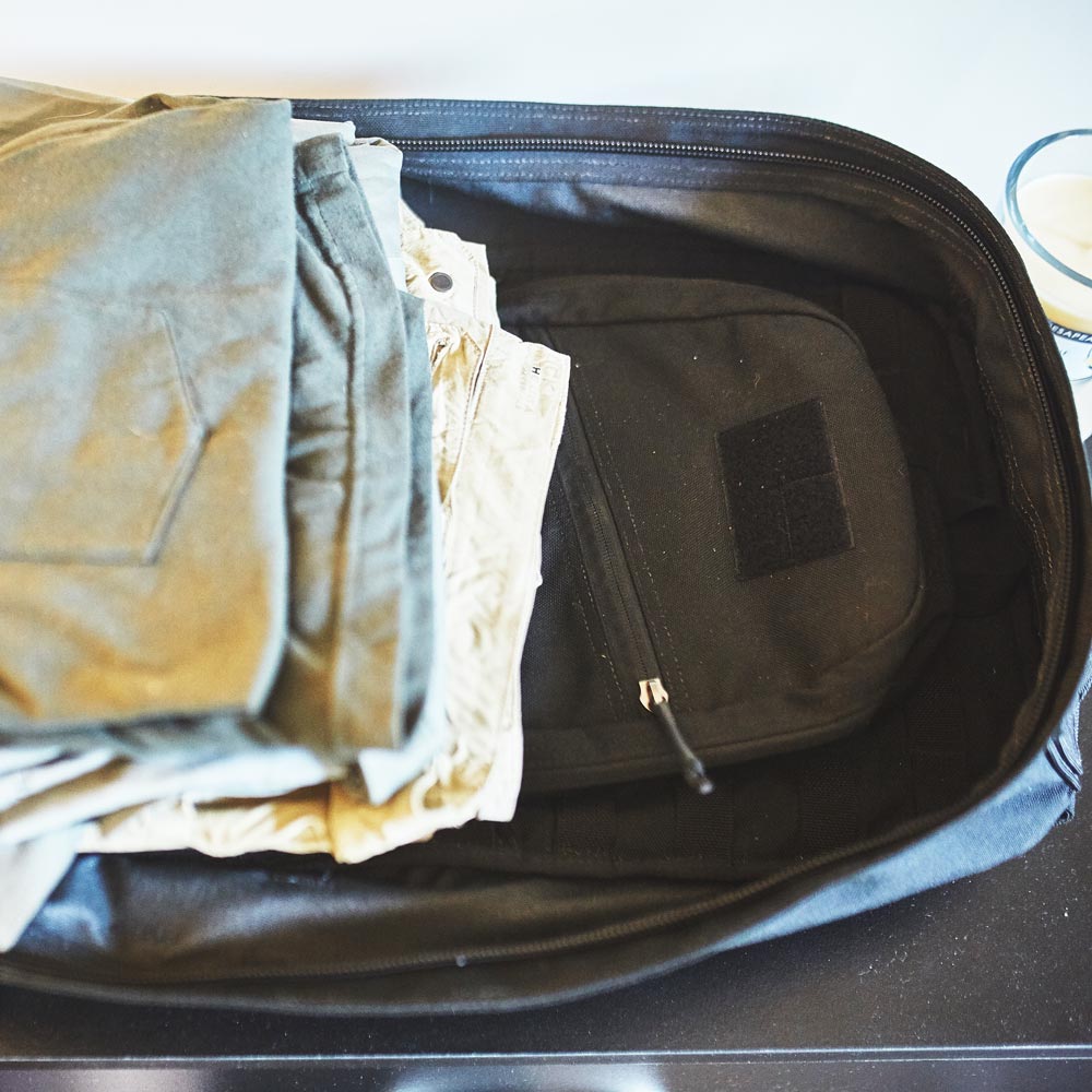 Open suitcase with neatly folded clothes and a black pouch inside, sitting on a dark surface.