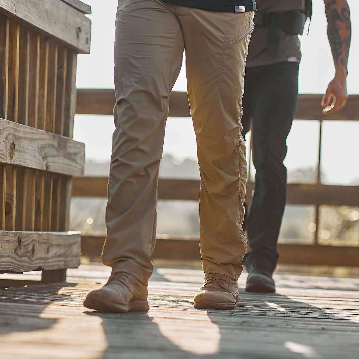 Two men walking on wooden bridge wearing rugged tactical pants and boots in outdoor setting
