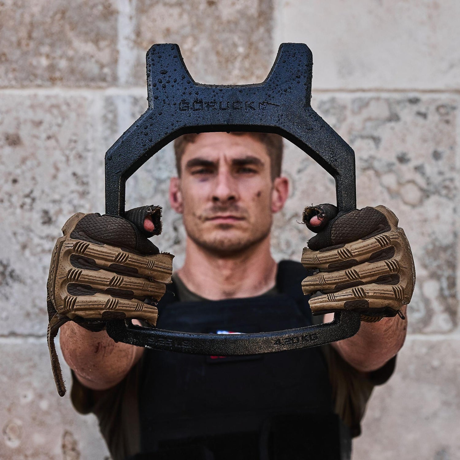 A man in tactical gloves holds a black metal tool, with his face blurred in the background.