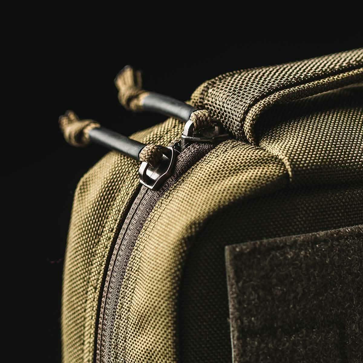 Close-up of durable olive green tactical rucksack zipper with reinforced paracord pulls against black background