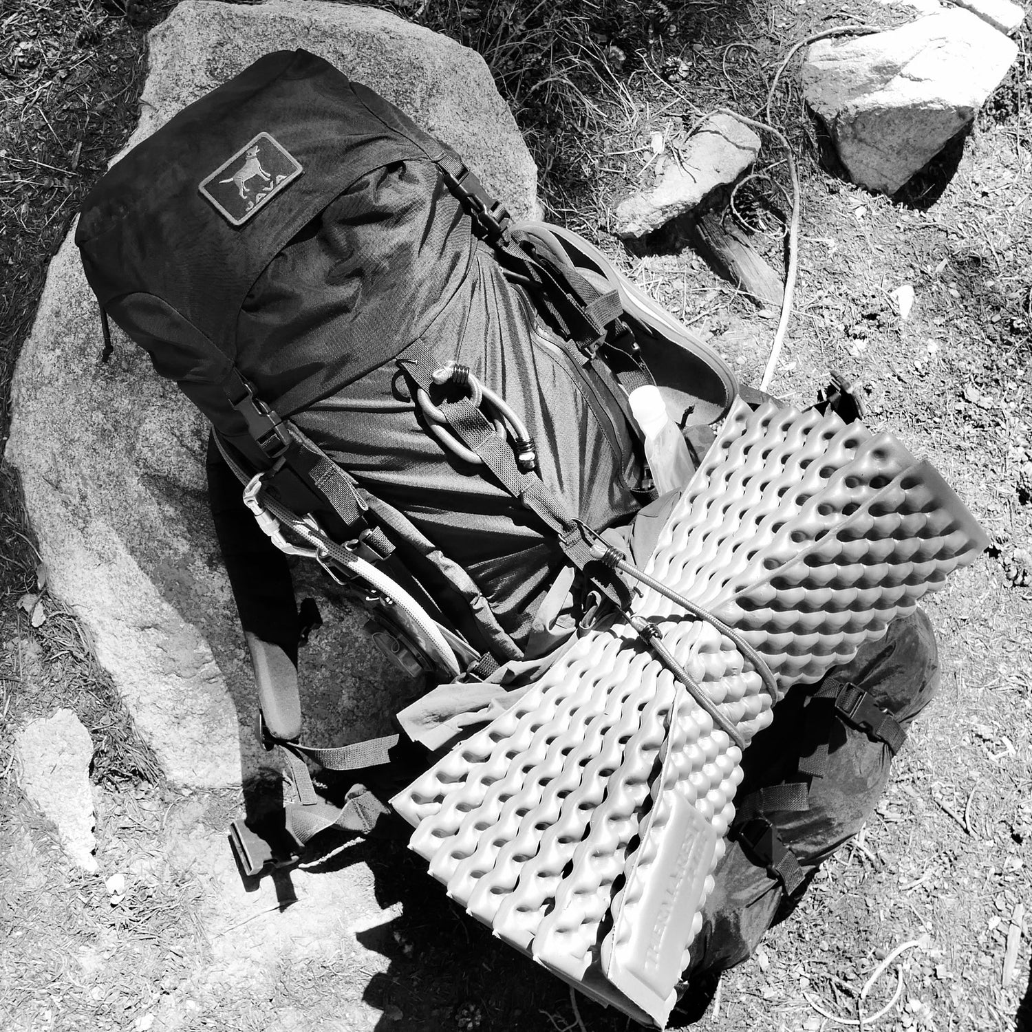 A GR MONSTER Bundle - PREORDER, featuring a spacious GORUCK rucksack with a foam sleeping pad attached, rests on a rock outdoors.
