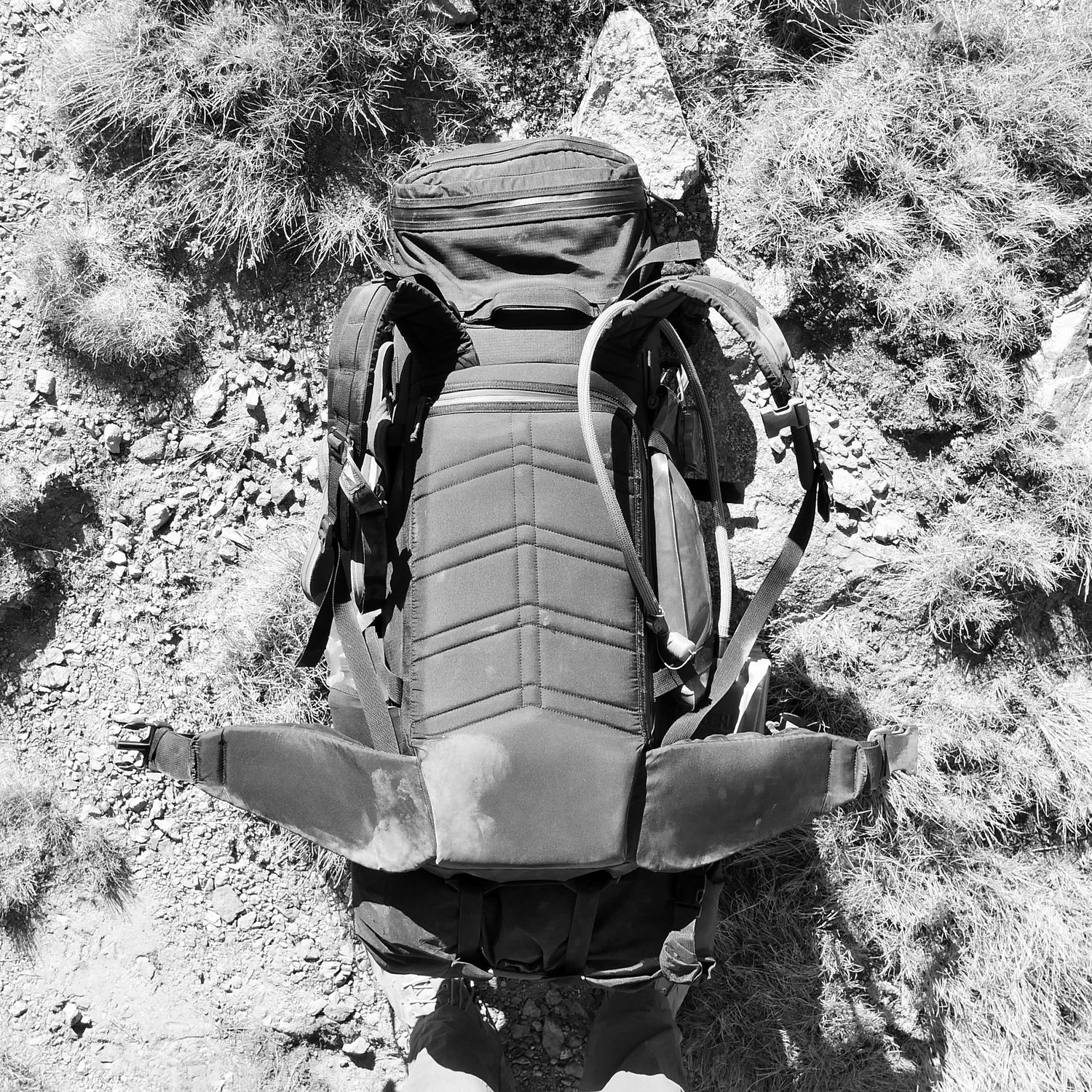 A GR MONSTER Bundle - PREORDER rests on rocky ground with tufts of grass, captured from above in black and white, evoking the rugged spirit of adventure.