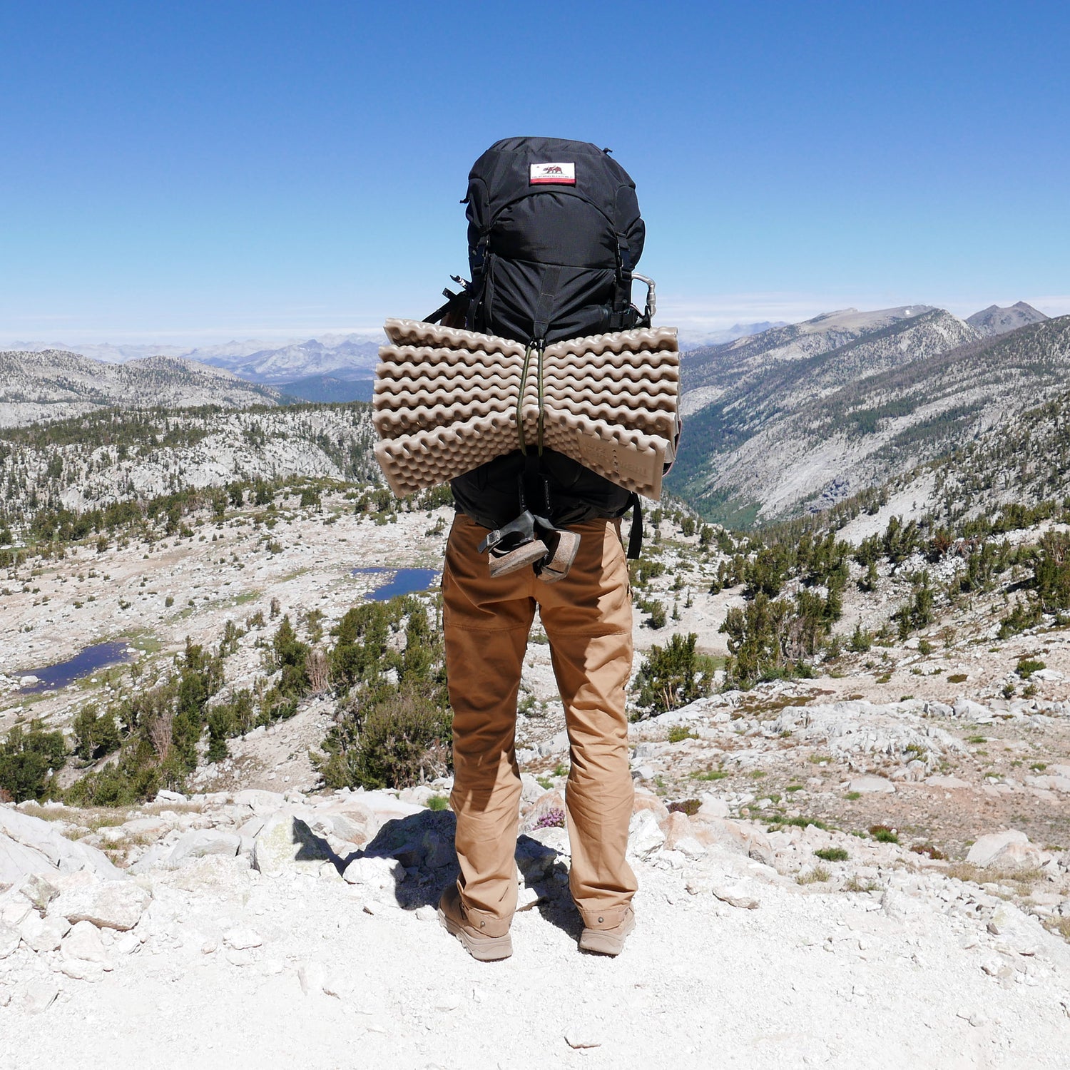 A hiker carrying the GR MONSTER Bundle - PREORDER stands on a rocky mountain overlooking a vast, scenic landscape.