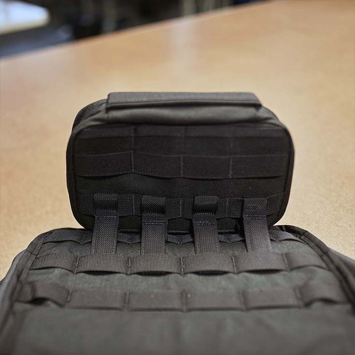 Close-up of a black tactical pouch with MOLLE webbing on a tan surface.