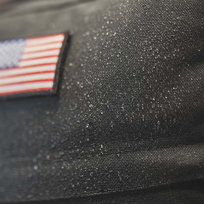 Close-up of a black fabric with water droplets and a small American flag patch.