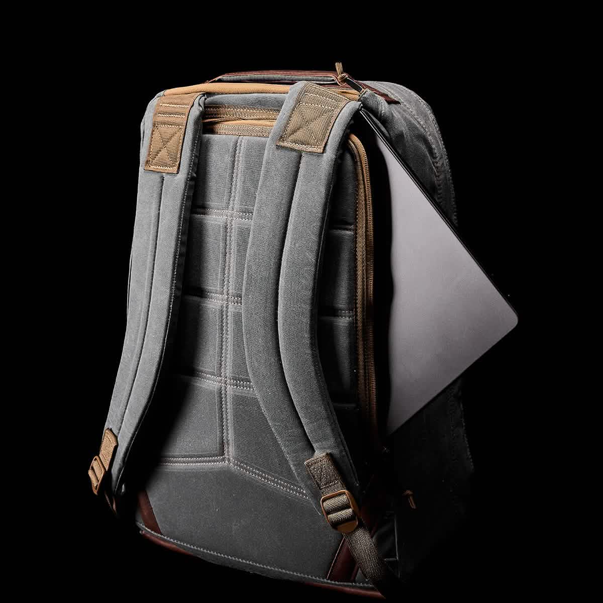 A GR1 USA - Heritage by GORUCK in gray, featuring padded straps and brown trim against a black background, is partially unzipped to showcase a laptop inside.