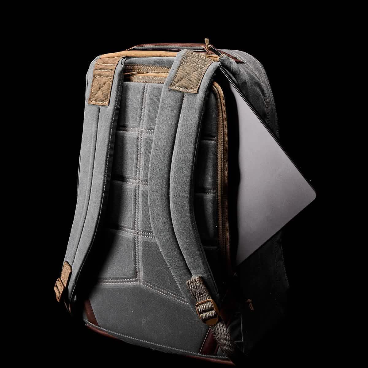 Back view of gray GORUCK backpack with padded straps and laptop partially inserted, black background