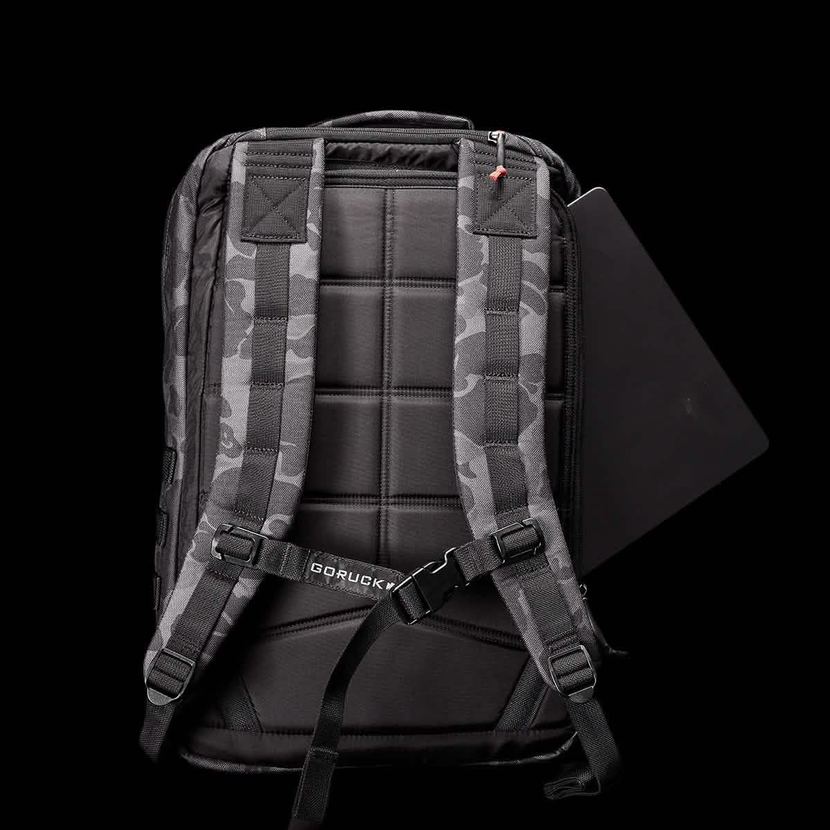 Back view of black Frogskin GORUCK rucksack with padded straps and laptop sleeve partially open on black background