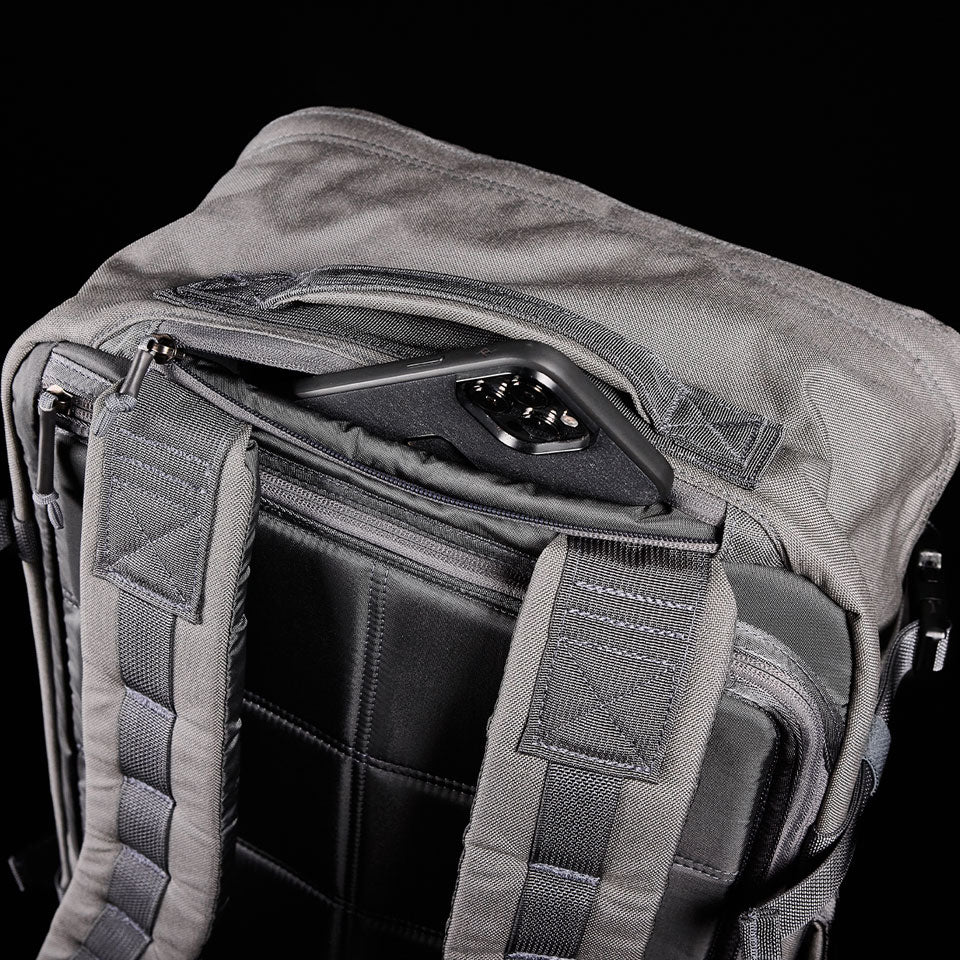 A phone is partially tucked into a zippered pocket on a gray backpack with padded shoulder straps.