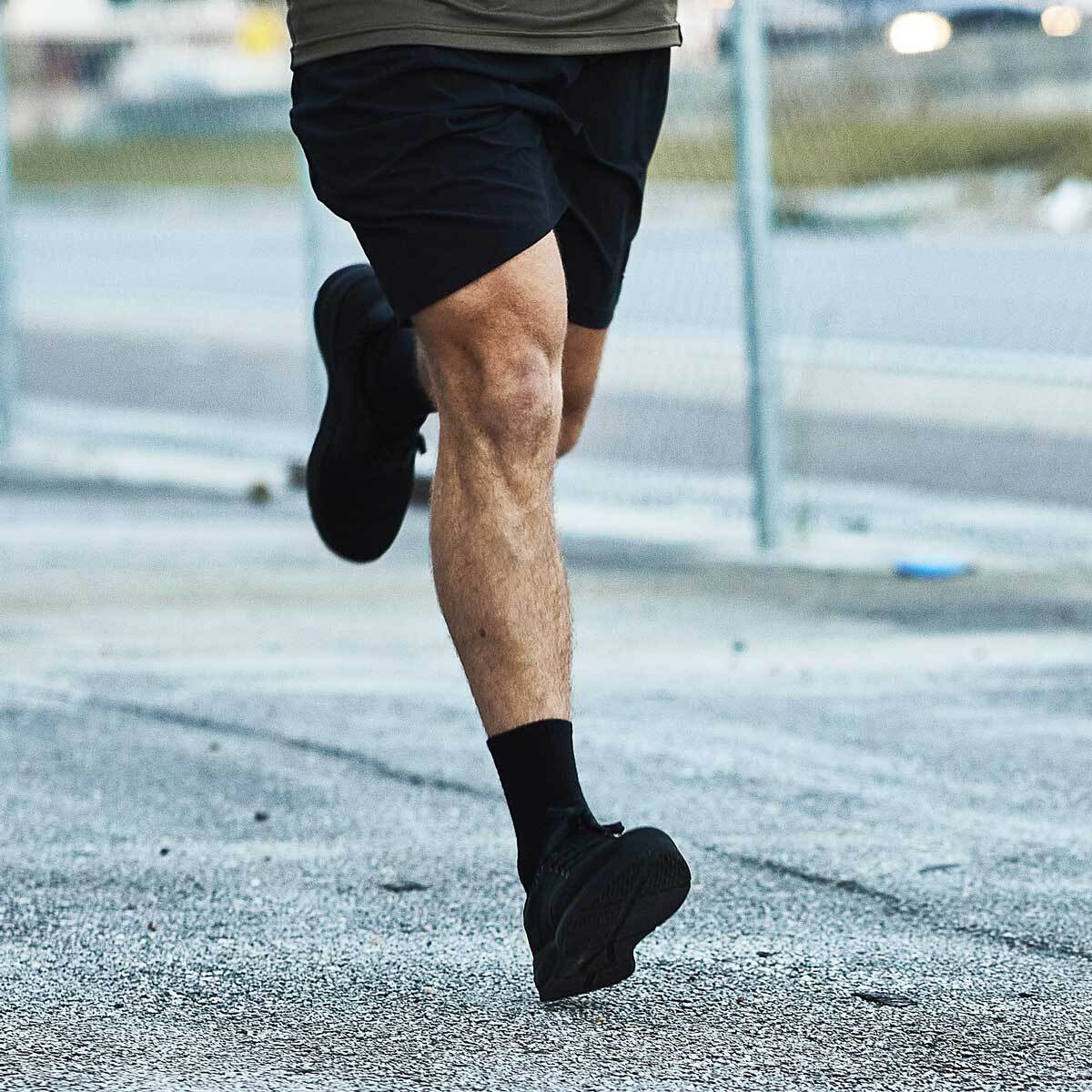 A person running outdoors, wearing black shorts, black socks, and black shoes.