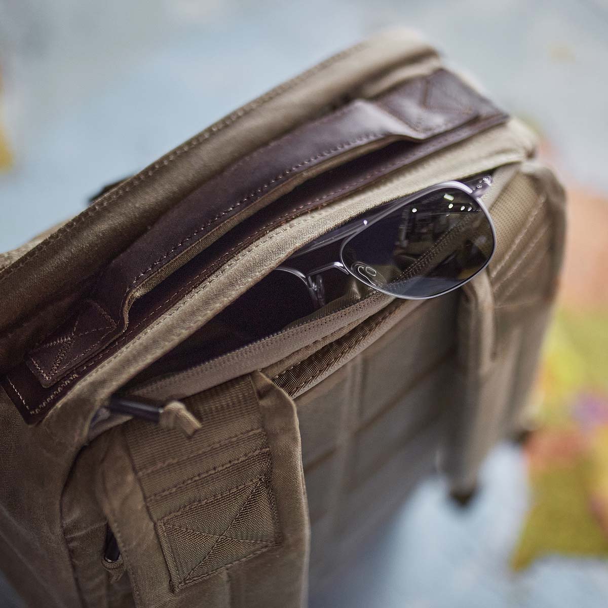 Brown backpack with sunglasses tucked into a zippered pocket on top, seen from above.