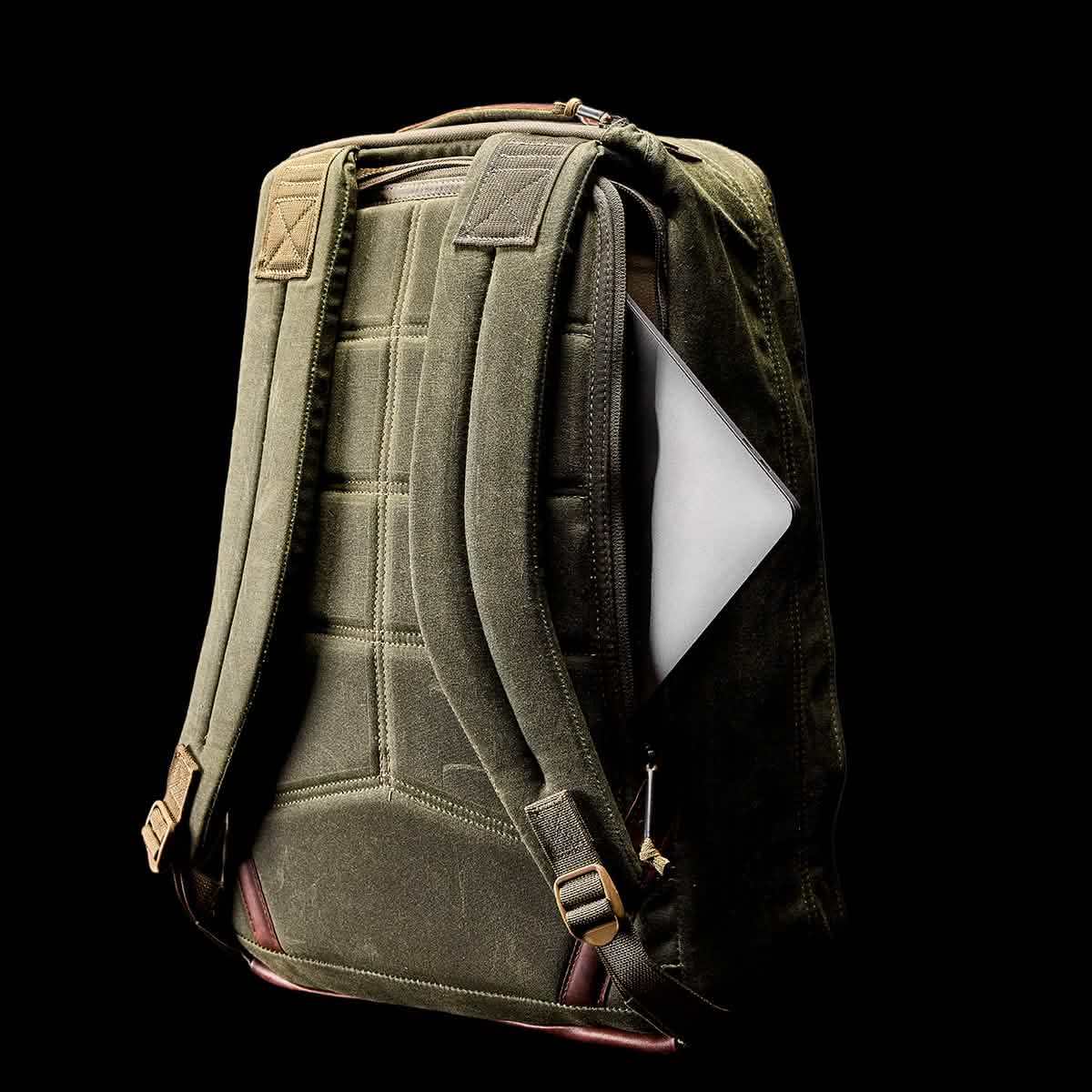 A GR1 USA - Heritage backpack from GORUCK, featuring padded shoulder straps, is slightly open to display a silver laptop inside. This retro green canvas rucksack is set against a black background.