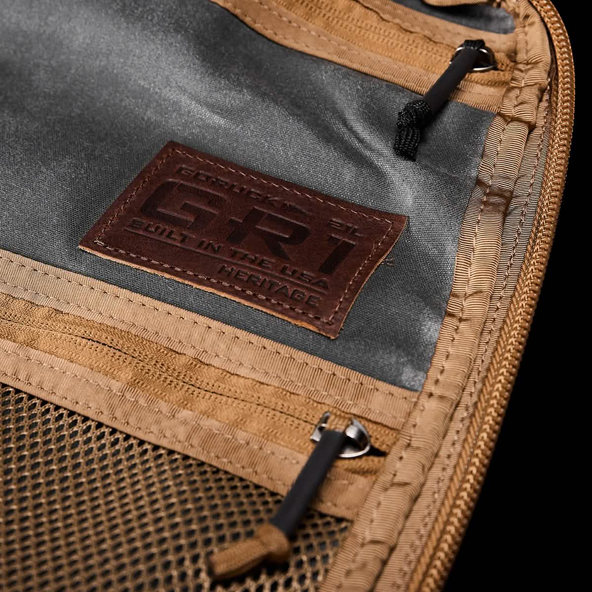 A close-up view of the GR1 USA - Heritage backpack interior reveals a brown leather patch labeled with the GORUCK brand. The interior is equipped with tan zippers, a mesh pocket, and features a dark fabric crafted from durable waxed canvas, enhancing its rugged rucksack appeal.