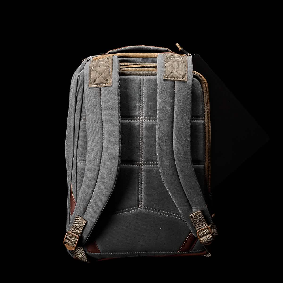 A rucksack in gray with brown accents, made from durable waxed canvas, is displayed against a black background. It features adjustable padded shoulder straps and a top handle, embodying the style of the GORUCK GR1 USA - Heritage.
