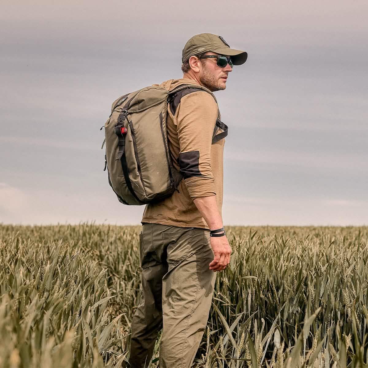 Man rucking outdoors wearing GORUCK backpack, cap, and sunglasses in grassy field