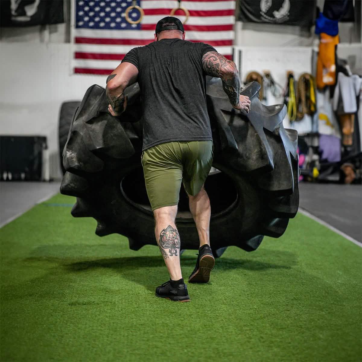 Man flipping heavy tire in gym with American flag and workout gear in background