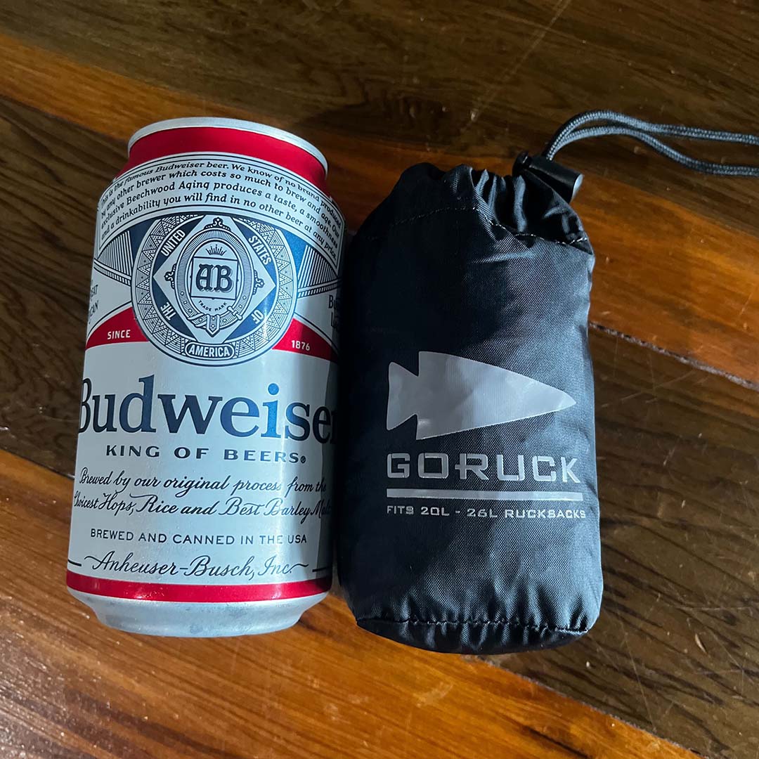 A Budweiser can next to a small, black, drawstring GORUCK bag on a wooden surface.
