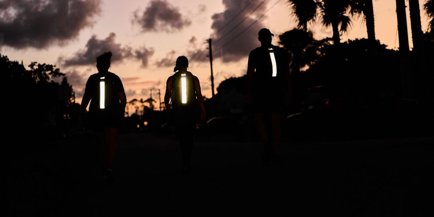 Three people walking at dusk wearing reflective vests; palm trees and clouds are visible in the background.