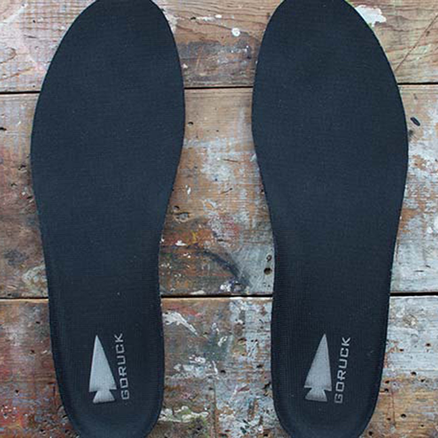 A pair of black GORUCK insoles on a worn wooden surface.