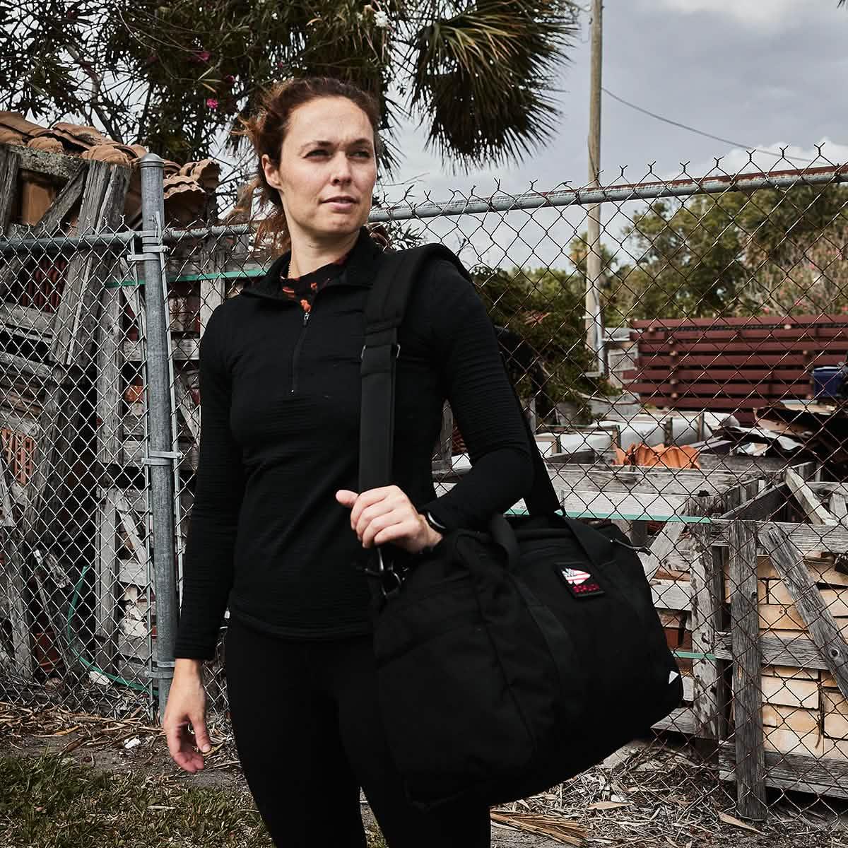 Woman outdoors carrying GORUCK rucking gear bag in rugged urban setting