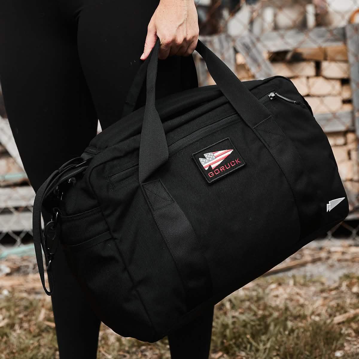 Person holding a black GORUCK rucking gear bag outdoors with visible GORUCK logo