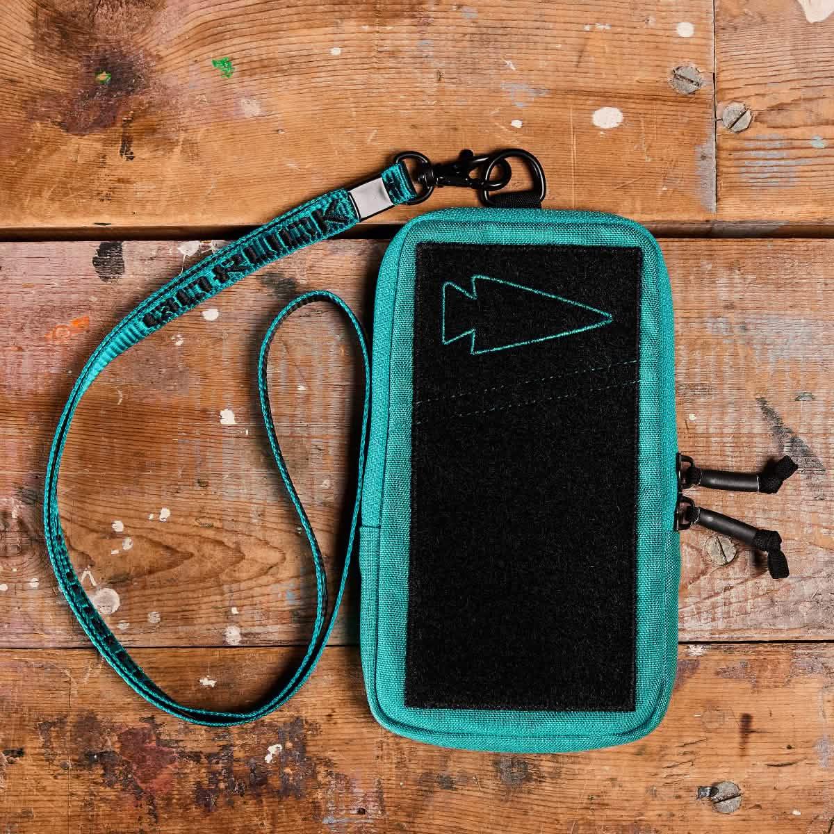 GORUCK teal lanyard with black arrow patch pouch on rustic wooden surface