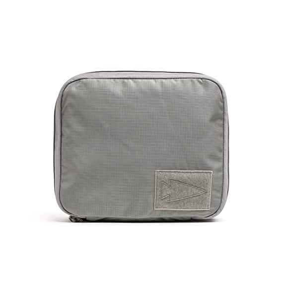The Shadow Pockets - Ripstop ROBIC® by GORUCK is a gray, rectangular travel pouch constructed from ROBIC Ripstop Nylon. It features a zipper and has a patch on the front with a simple arrow design. Ideal for organizing lightweight gear, the subtly textured fabric offers durability and enhances rucksack organization.